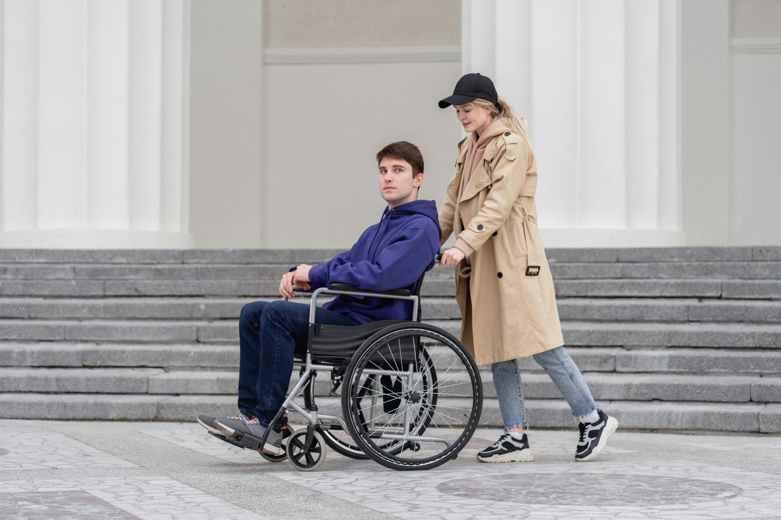 Man in wheelchair and woman outdoors, sharing a moment on urban steps. Embracing togetherness and mobility.