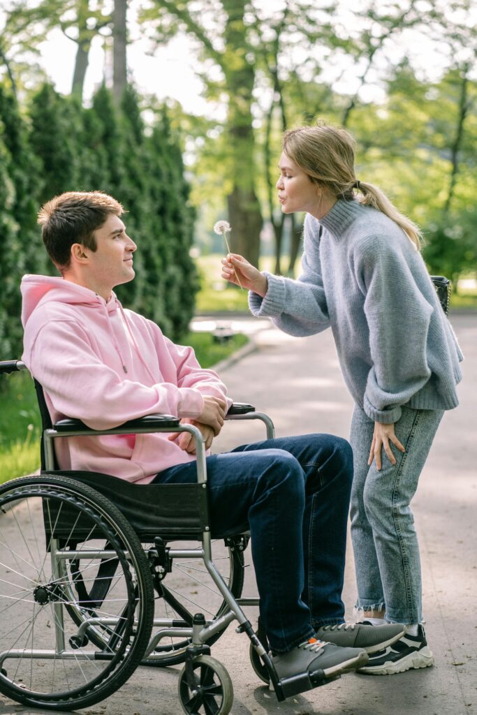 Happy couple outdoors with woman blowing dandelion and man in wheelchair.